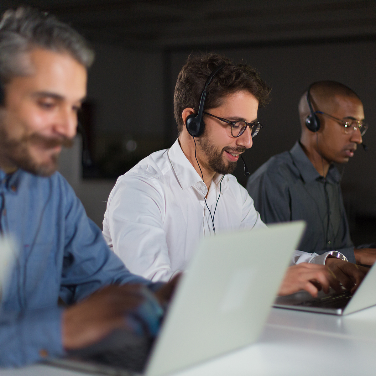 Three professionals wearing headsets engaged in a call center environment, using laptops to manage customer interactions and enhance communication solutions.