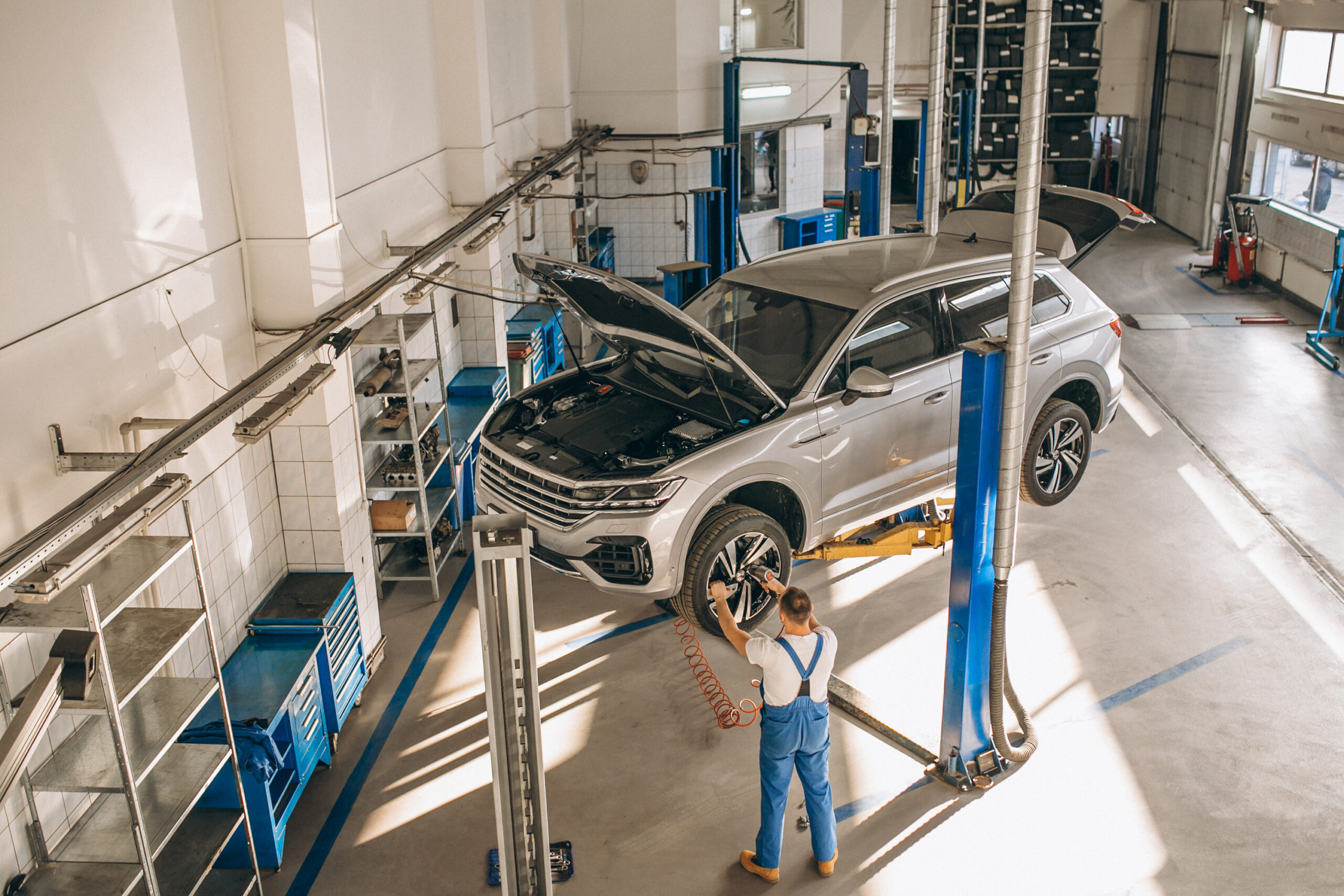 Auto mechanic inspecting a lifted silver SUV in a well-lit auto care shop, highlighting Merlin Complete Auto Care's automotive services.